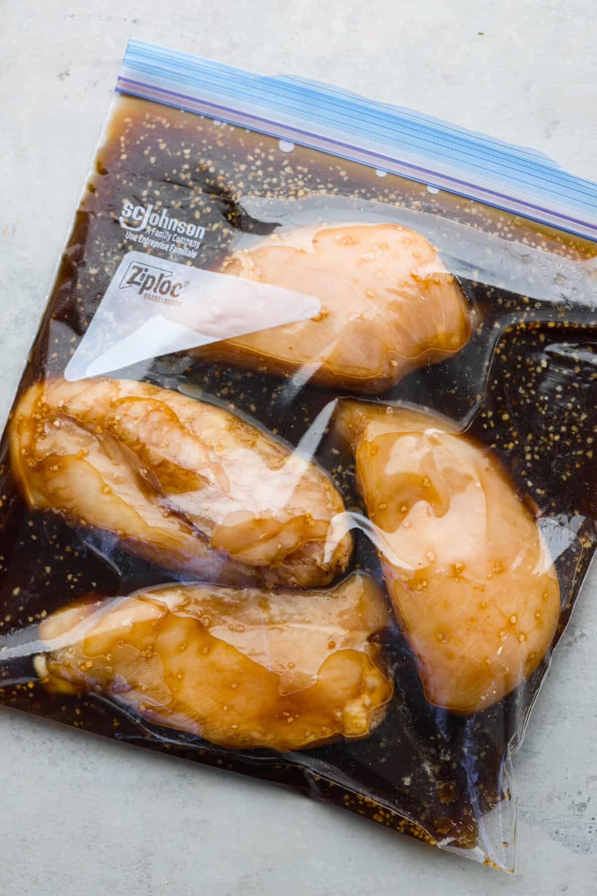 4 raw chicken breasts marinating in a bag filled with bourbon marinade.