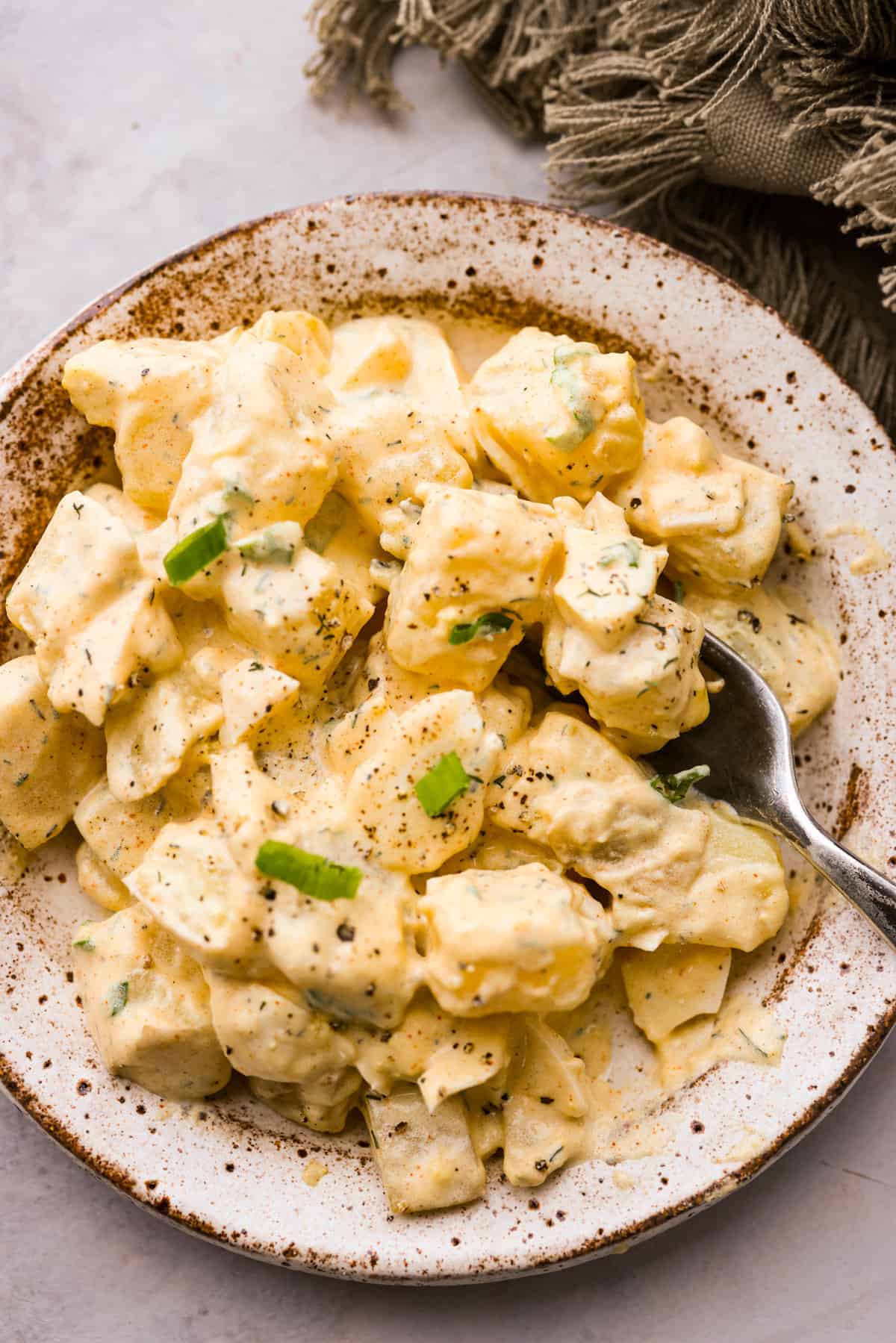 This classic potato salad recipe is cool, creamy, and the perfect side dish for any cookout! Easy to make ahead and so flavorful! A serving of potato salad on a stoneware plate.