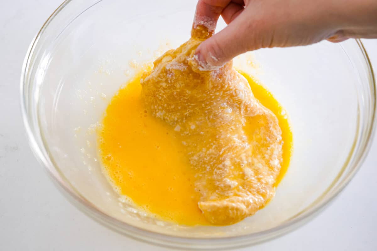 Coating the chicken in a beaten egg mixture.
