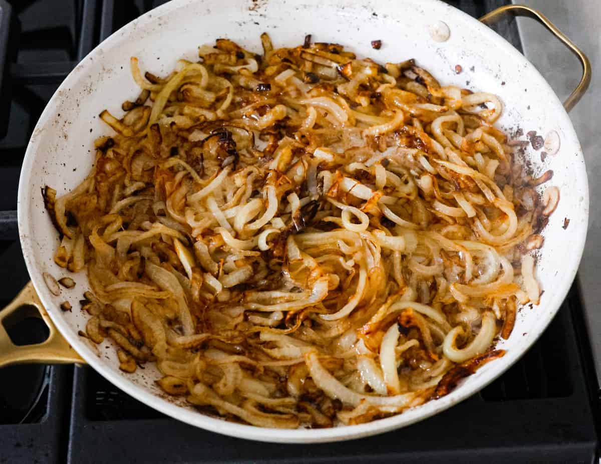 French Onion Pork Chops have all of the wonderful flavors of the classic soup in pork chop form! Caramelized onions and seared pork chops are joined with a savory sauce and two types of cheese for an amazing meal. Everything is cooked in one pan for a quick and easy weeknight dinner! The first step, caramelizing the onions in a white skillet.