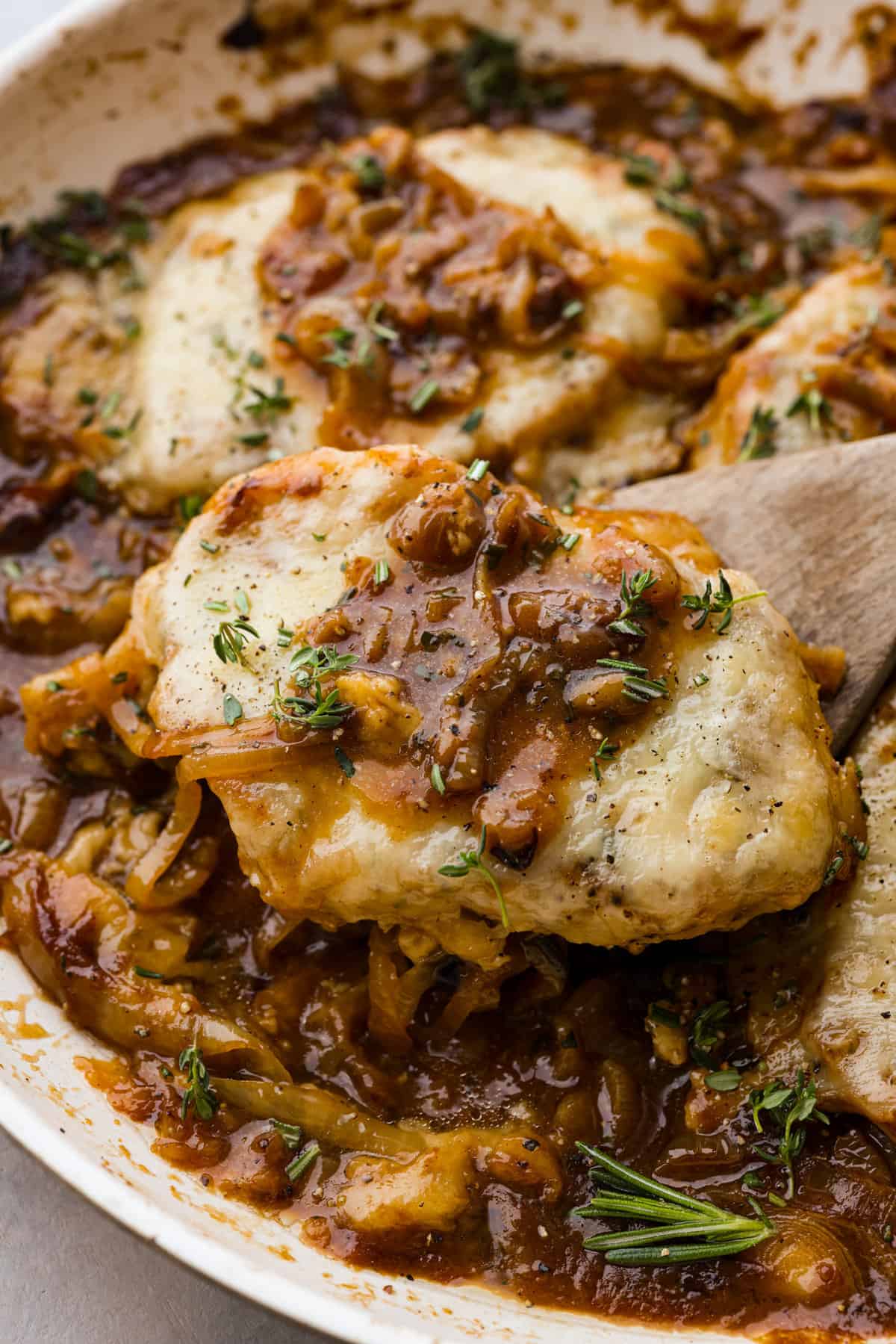 French Onion Pork Chops have all of the wonderful flavors of the classic soup in pork chop form! Caramelized onions and seared pork chops are joined with a savory sauce and two types of cheese for an amazing meal. Everything is cooked in one pan for a quick and easy weeknight dinner! A French onion pork chop on a wooden spoon