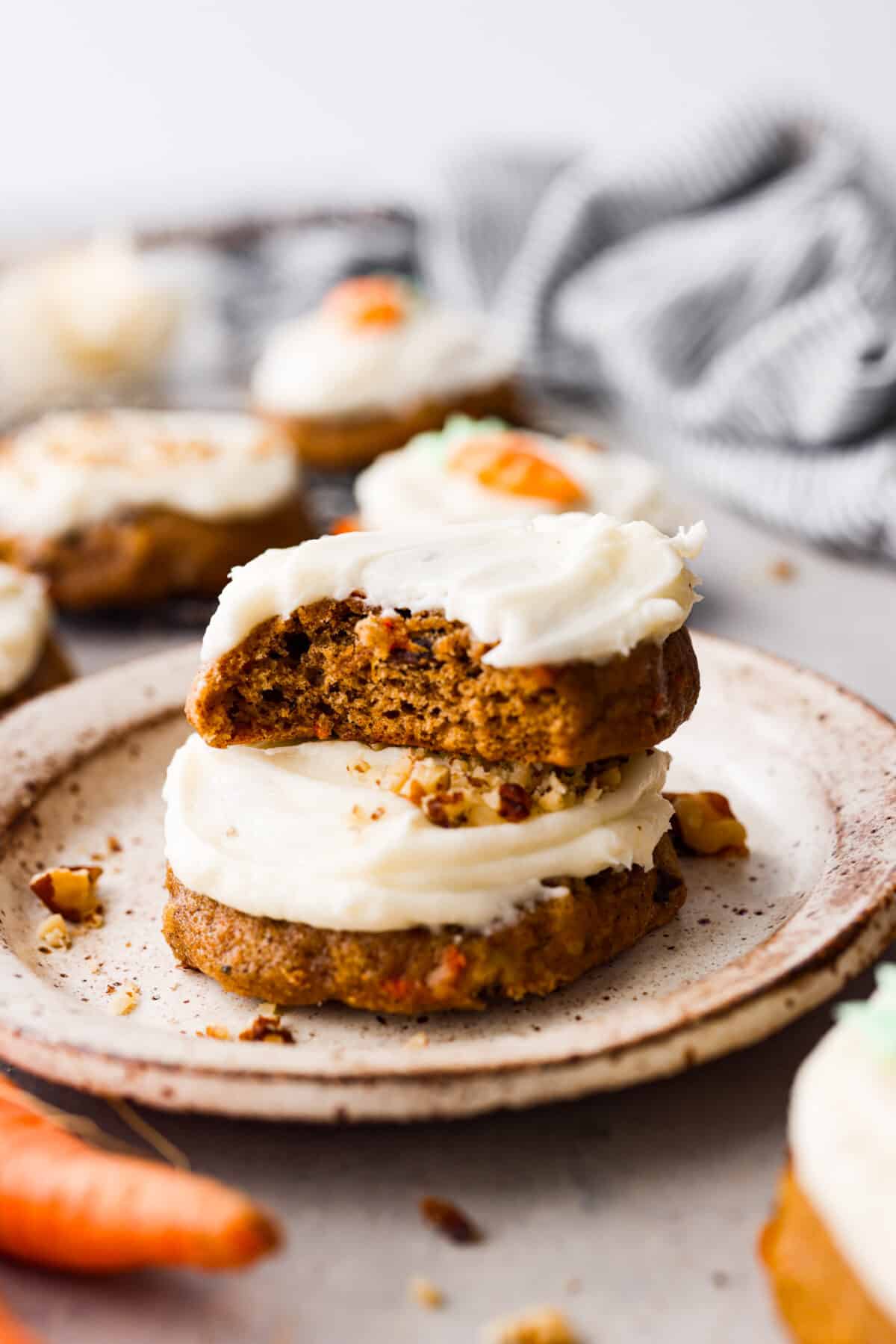 2 frosted carrot cake cookies stacked on top of each other. One has a bite taken out of it.