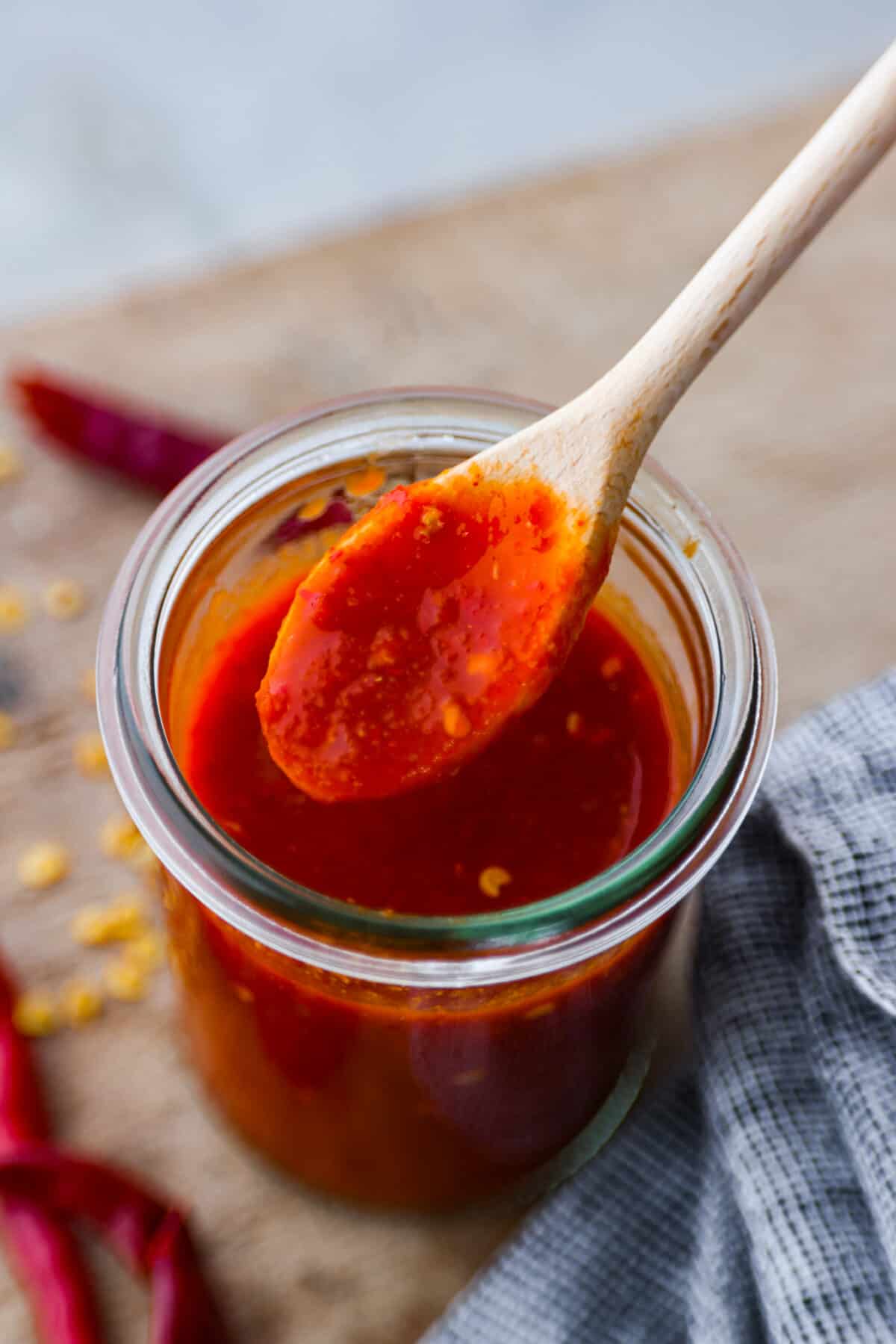 Homemade hot sauce in glass jar, being mixed with a wooden spoon.