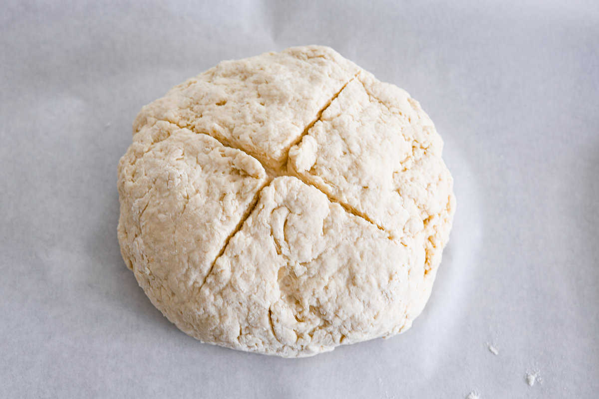 This Irish soda bread recipe uses just 4 pantry staples for a warm, crusty loaf that's perfect for slathering with butter and jam, or soaking up your favorite soup. No kneading required! An unbaked soda bread loaf, shaped and ready to be put in the oven.