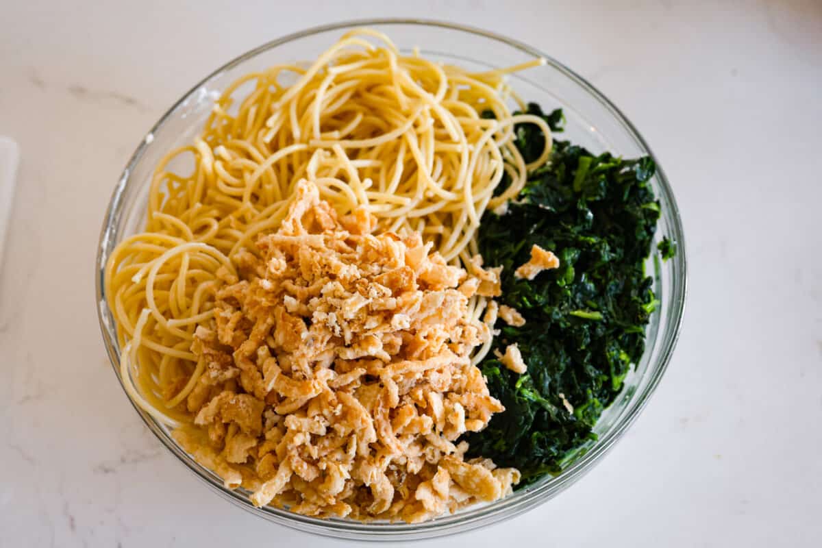 Second process photo of spaghetti noodles, fried onions, and spinach in a bowl.