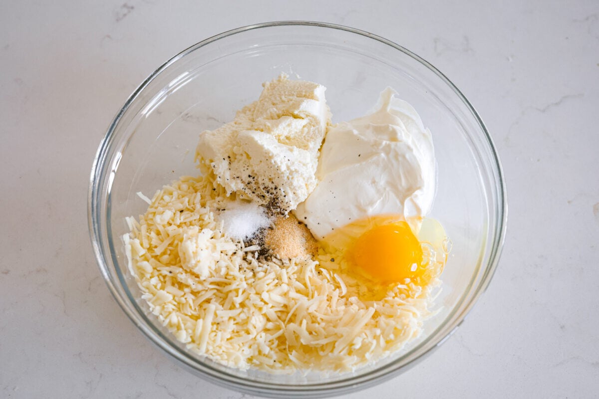 Third process photo of the cheese, sour cream, egg, and ricotta cheese added to a bowl.