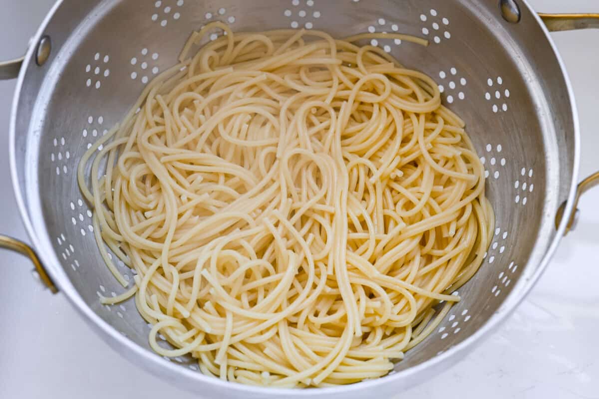 First process photo of the spaghetti cooked and straining.
