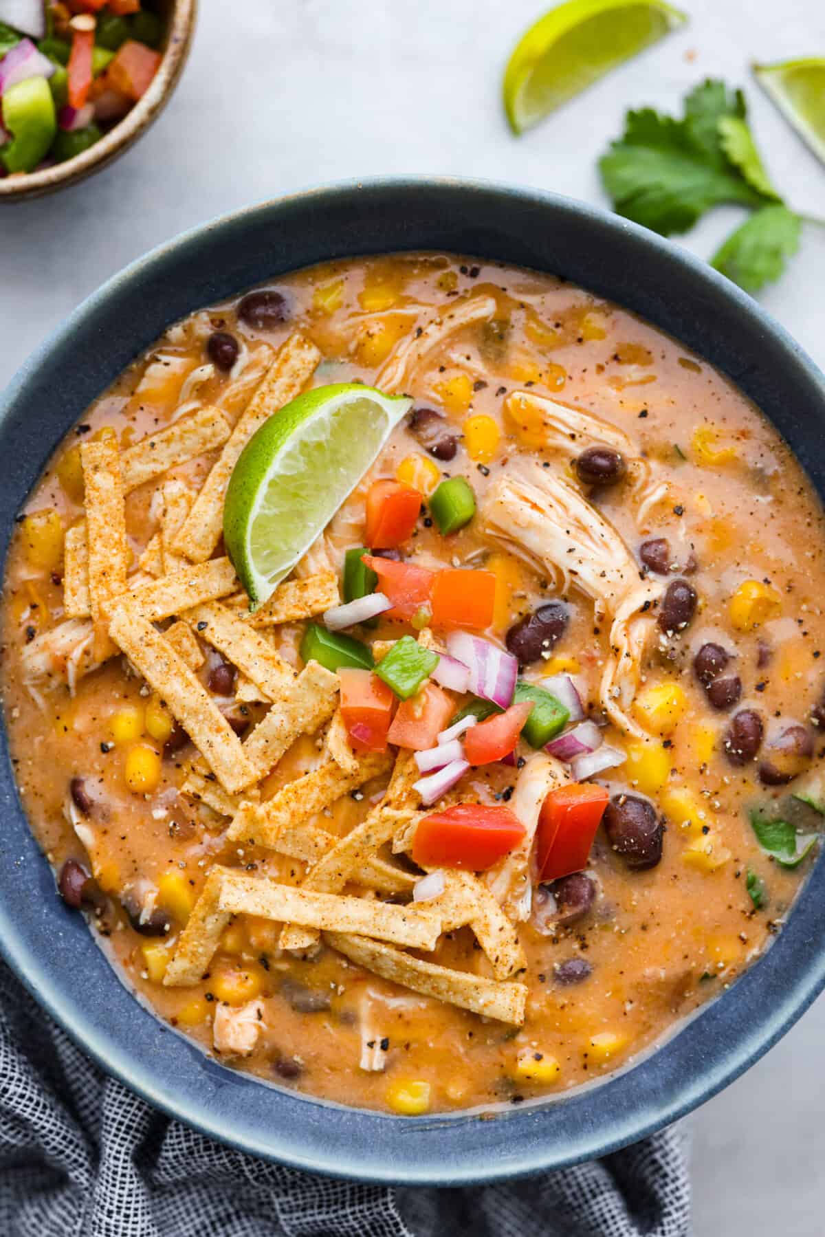 A serving of chicken fajita soup, topped with tortilla strips, diced tomatoes, and a lime wedge.