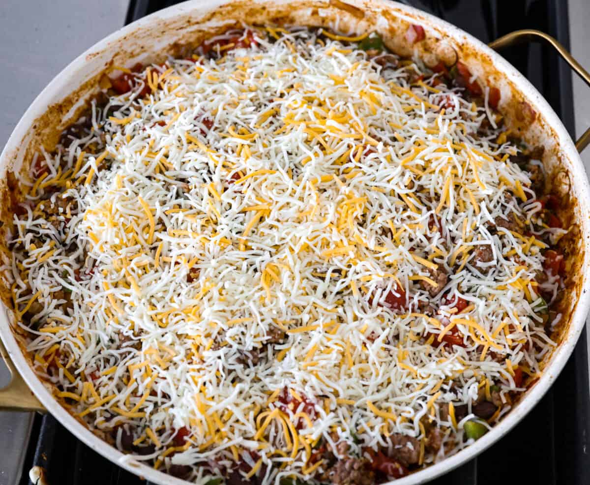 The taco skillet being topped with shredded cheese.