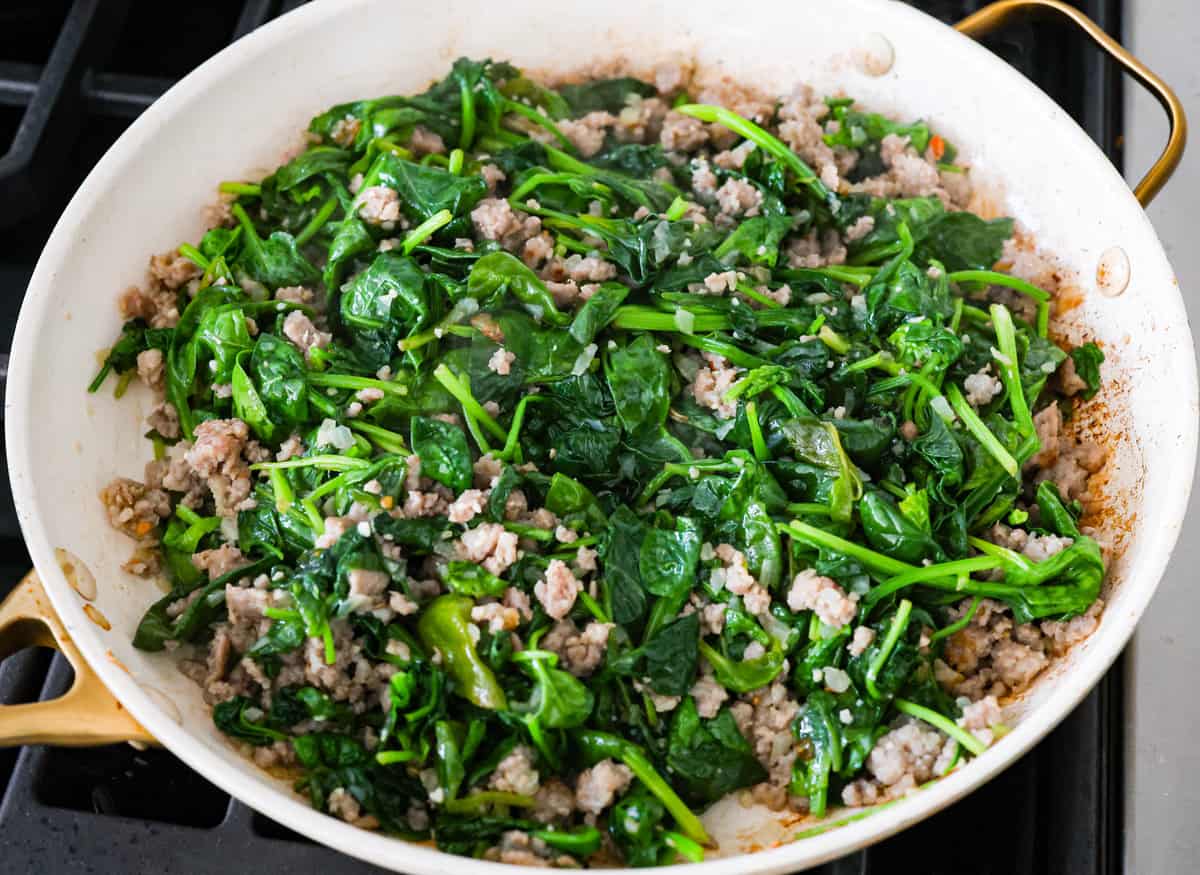 This white lasagna recipe swaps out traditional marinara for a homemade alfredo sauce that’s too good to resist. Packed with tender spinach, ricotta cheese, and Italian sausage, each bite is a dream! The sausage and spinach being cooked together in a skillet.