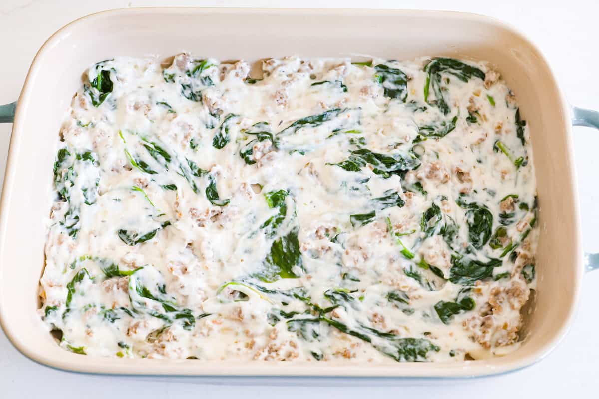 This white lasagna recipe swaps out traditional marinara for a homemade alfredo sauce that’s too good to resist. Packed with tender spinach, ricotta cheese, and Italian sausage, each bite is a dream! Adding the white sauce layer to a baking dish.
