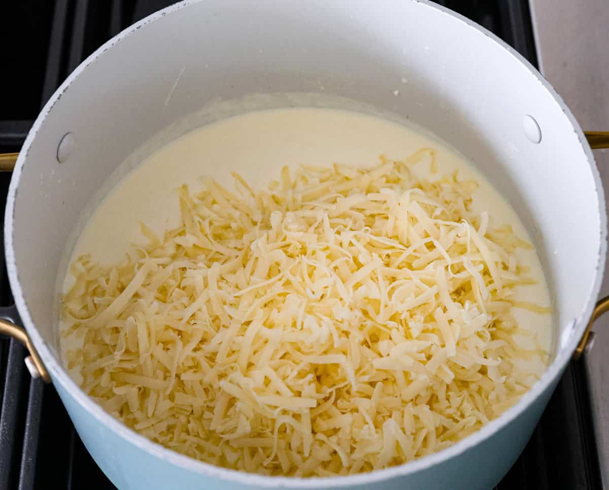White Cheddar Mac and Cheese is super creamy and filled with rich, decadent flavor. This pasta recipe is the perfect comforting side dish for potlucks, holidays or even weeknight dinners! The cheesy sauce being melted together in a large pot.