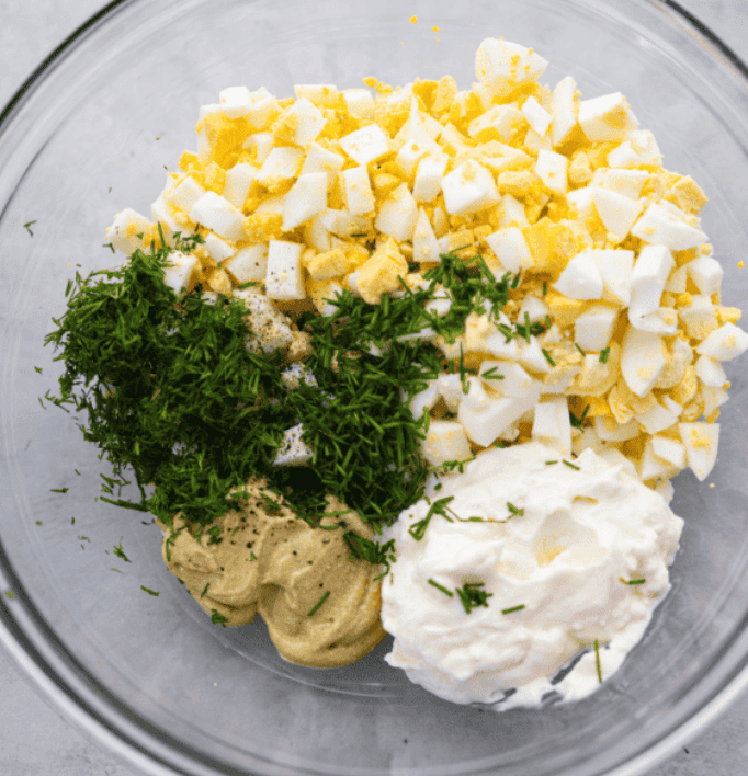 A glass bowl with egg salad ingredients ready to be mixed together. 