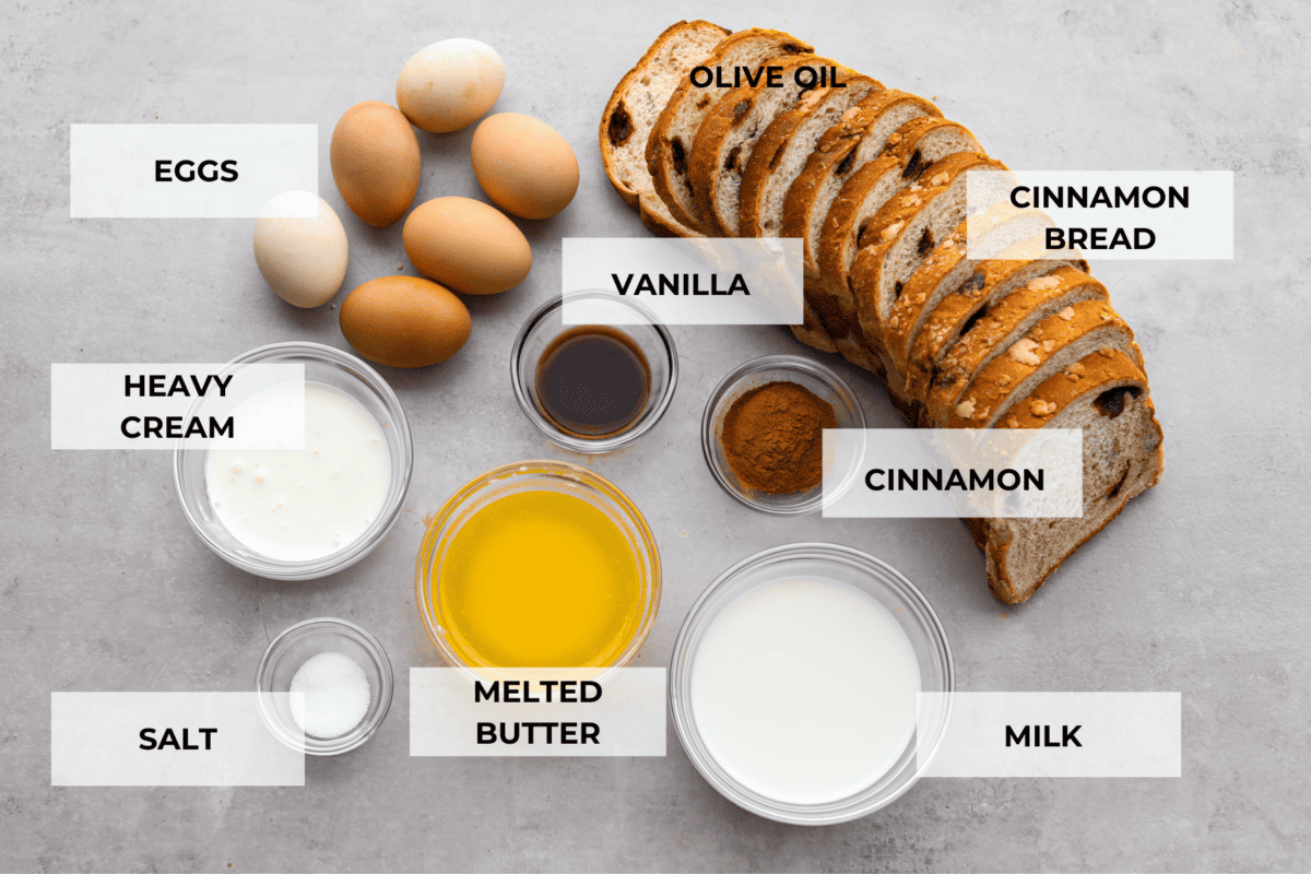 All of the French toast ingredients laid out. Listed are: eggs, heavy cream, salt, melted butter, milk, vanilla, cinnamon, and cinnamon bread.