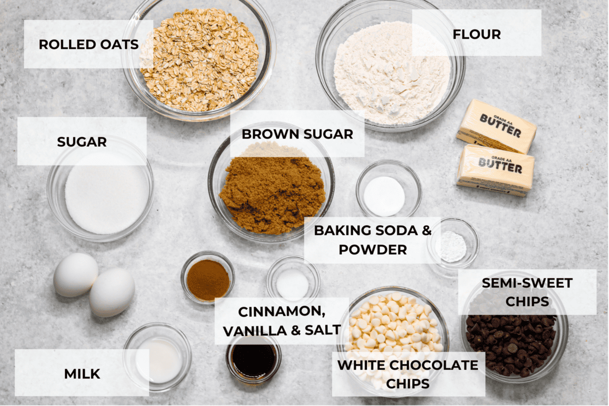 All of the marry me cookie ingredients in glass bowls. Listed are: rolled oats, flour, sugar, brown sugar, baking soda and powder, semi sweet chips, white chocolate chips, cinnamon, vanilla, salt, and milk.