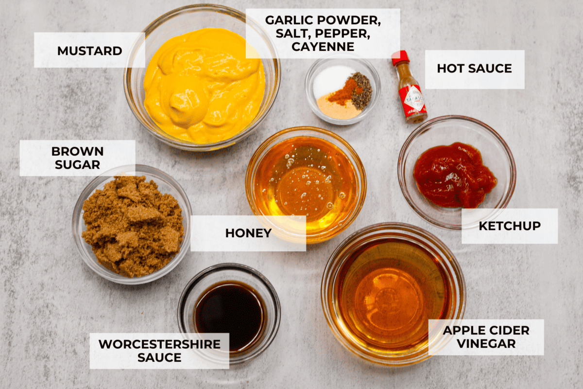 All of the ingredients for the sauce separated into individual glass bowl. Listed are: mustard, garlic powder, salt, pepper, cayenne, hot sauce, brown sauce, honey, ketchup, worcestershire sauce, and apple cider vinegar.