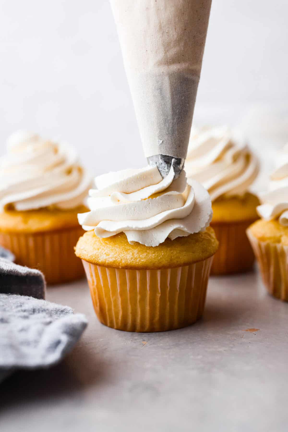 Piping Swiss meringue buttercream onto a vanilla cupcake.
