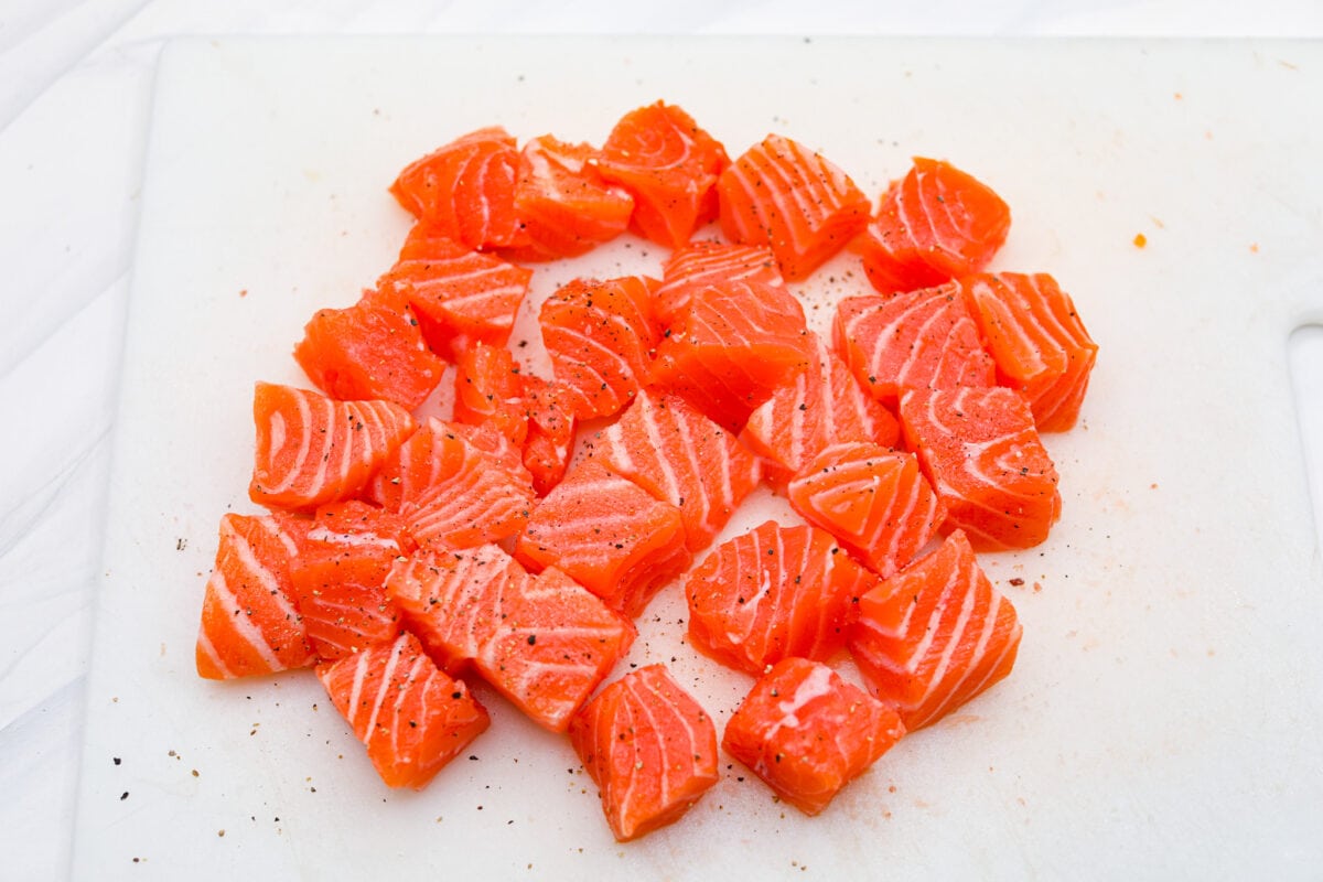 First photo of the salmon cut into bite-sized pieces. Second photo of the marinade mixed in a glass bowl. Third photo of the salmon marinating in the marinade. Fourth photo of the salmon bites lined in the air fryer before cooking.