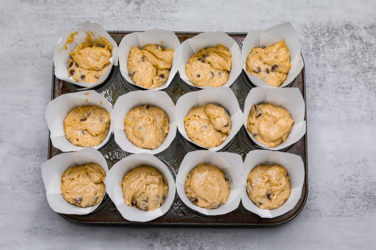 Chocolate chip muffin batter in a muffin tin filled with white muffin liners. 