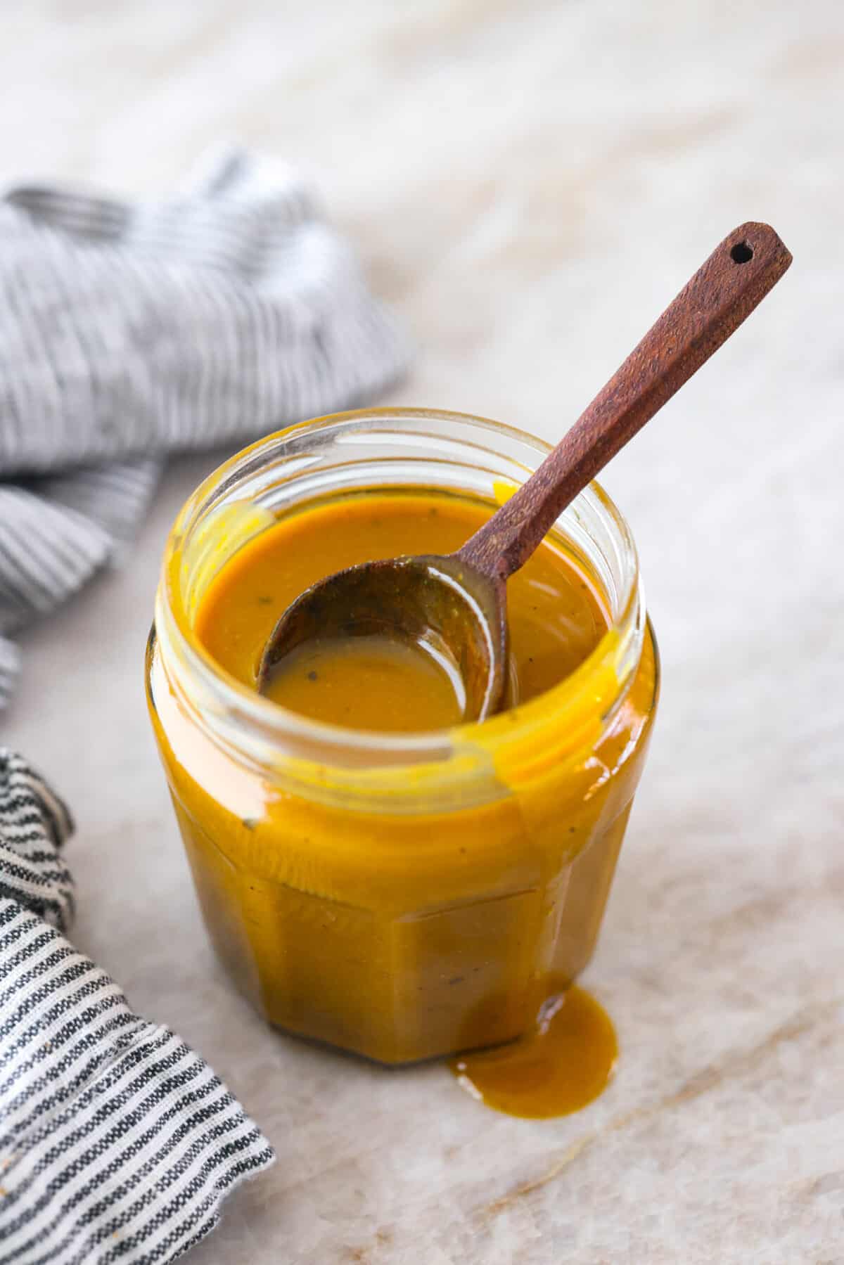 A glass jar filled with mustard bbq sauce. There is a wooden spoon in the jar as well.