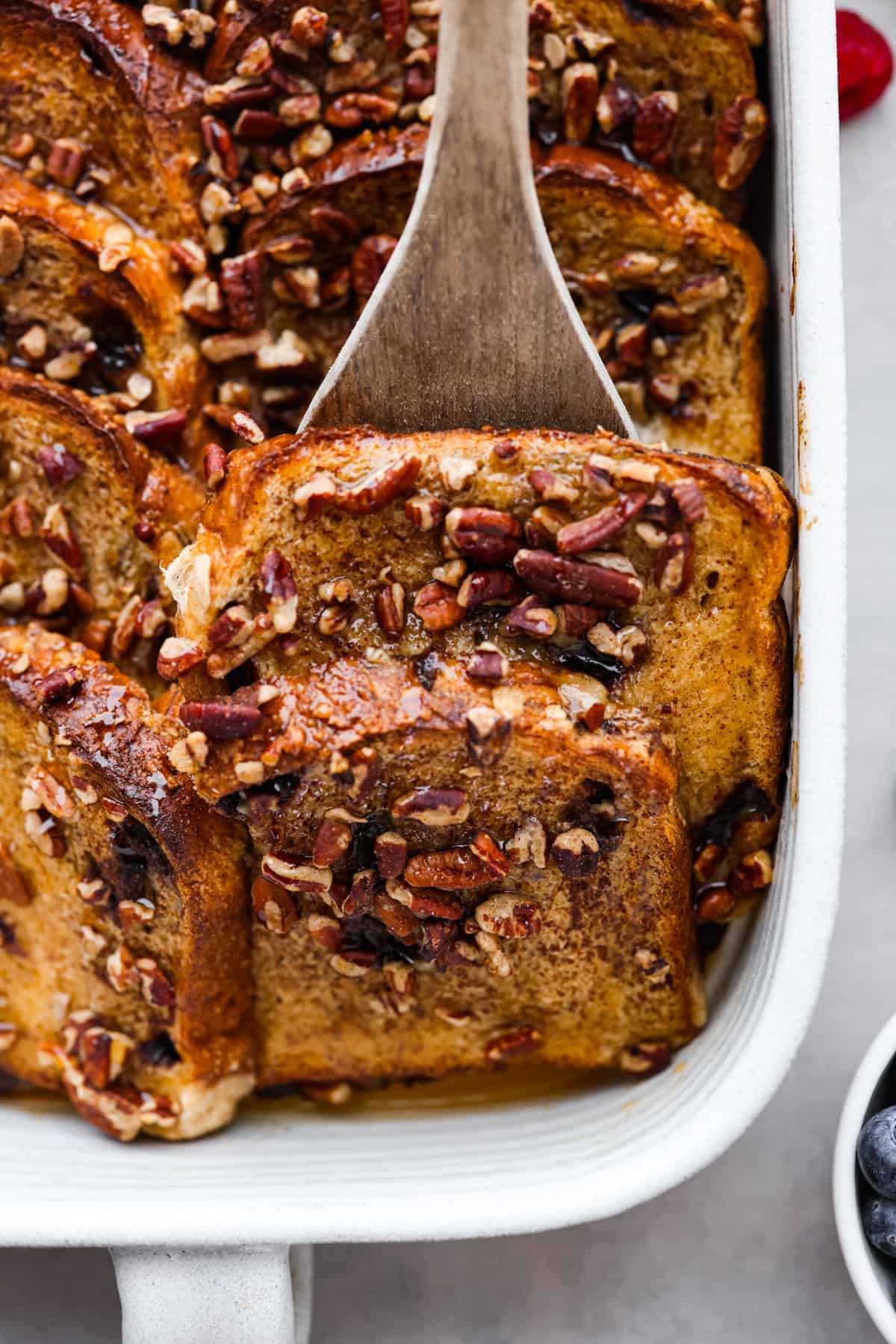 Cinnamon French toast bake is a warm and satisfying breakfast that's loaded with soft and sweet spiced bread all drizzled in maple syrup. Your family will go crazy over this insanely delicious (and easy-to-make) breakfast! Serving a slice of French toast with a wooden spatula.
