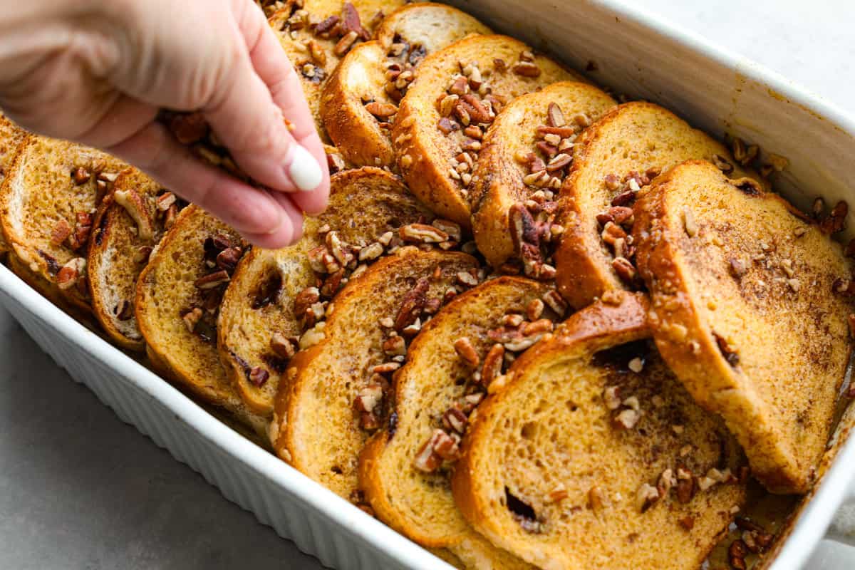 Cinnamon French toast bake is a warm and satisfying breakfast that's loaded with soft and sweet spiced bread all drizzled in maple syrup. Your family will go crazy over this insanely delicious (and easy-to-make) breakfast! Topping the cinnamon French toast bake with pecans.