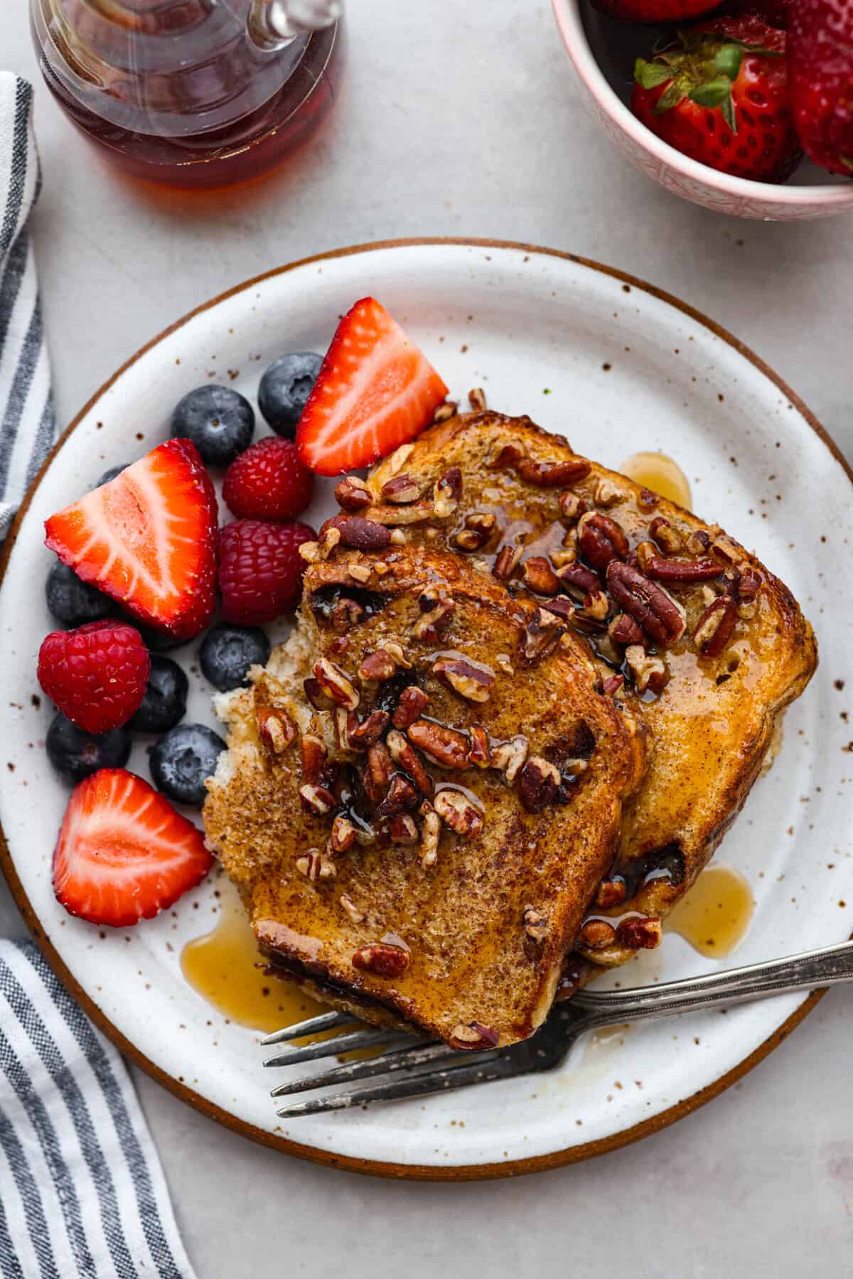 Cinnamon French toast bake is a warm and satisfying breakfast that's loaded with soft and sweet spiced bread all drizzled in maple syrup. Your family will go crazy over this insanely delicious (and easy-to-make) breakfast! A serving on a stoneware plate, surrounded by fresh berries.