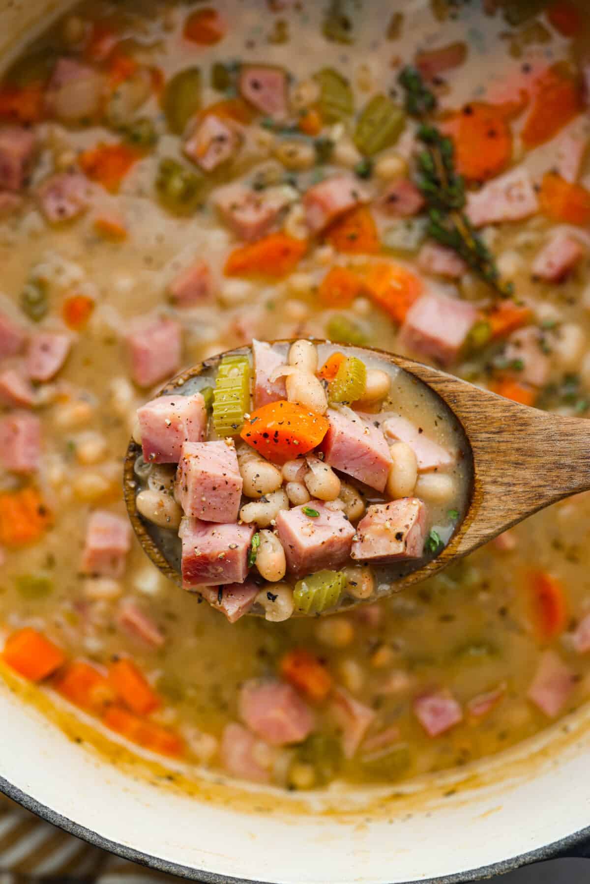 Close view of a wooden spoon lifting up a spoonful of ham and bean soup.