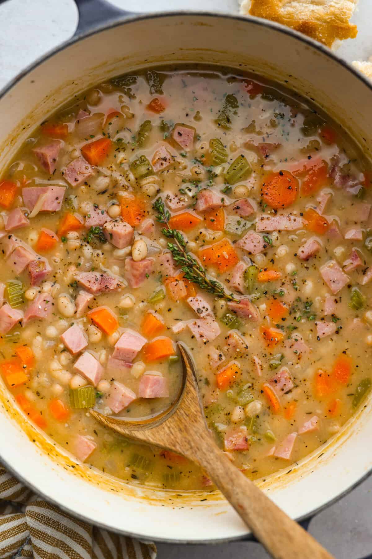 Top view of ham and bean soup in a large stock pot with a wooden spoon and garnished with thyme.