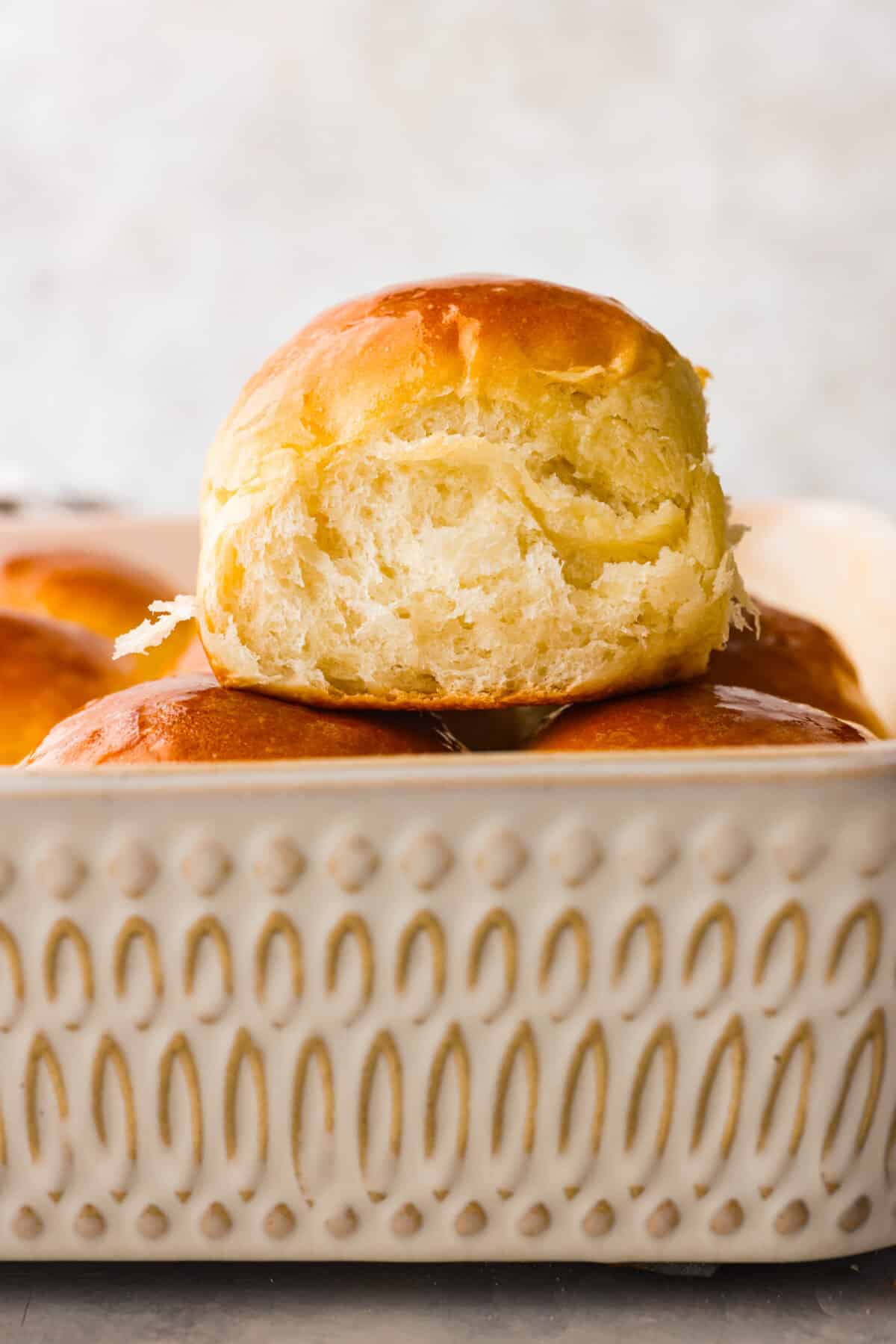 Close view of a perfectly soft buttery roll stacked on top of the pan of fresh baked rolls.