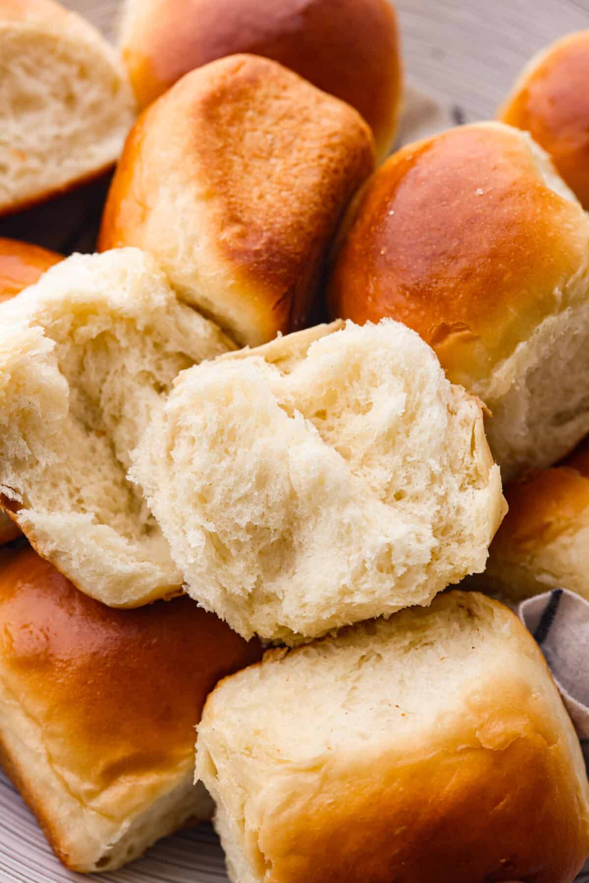 Close view of a perfect soft and buttery roll split open on top of a pile of rolls.
