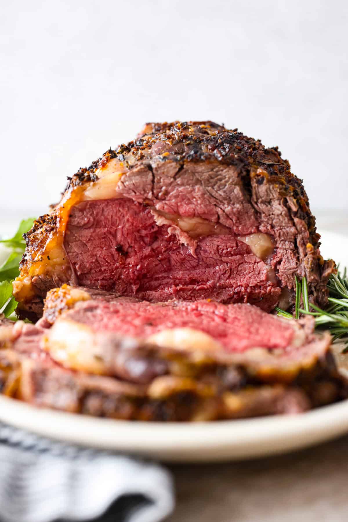 Close view of ribeye roast on a platter with herbs.