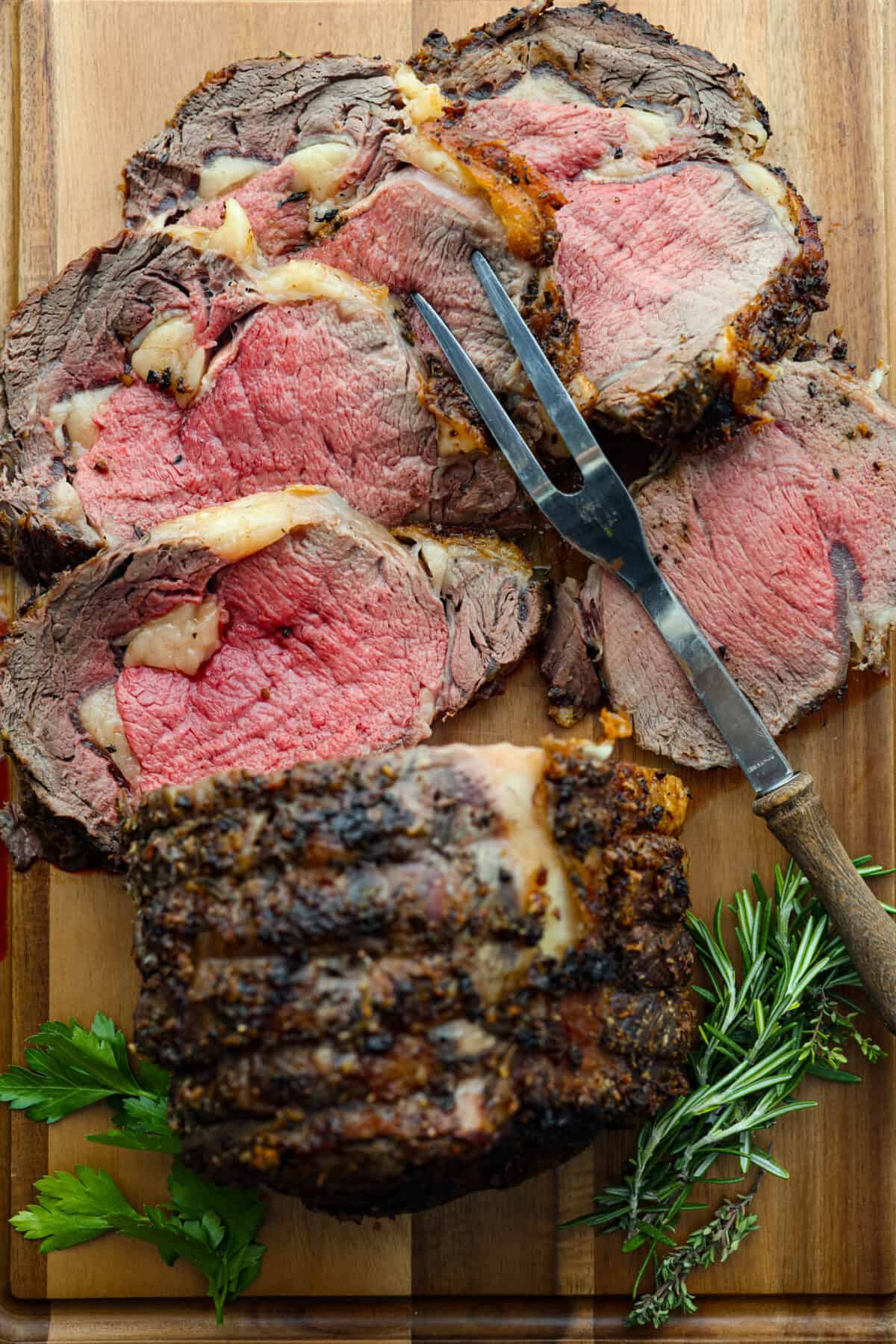 Top view of sliced ribeye roast on a wood cutting board with a large serving fork.