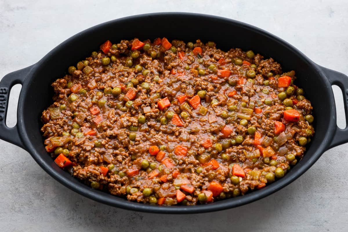 Preheat the oven to 375 degrees Fahrenheit. In a large, deep skillet, heat the oil over medium-high heat and cook the carrots, celery, and onion until softened, about 5 minutes. Add the beef and cook until thoroughly browned and no pink remains. Break it up into pieces as it cooks. Add the minced garlic and cook for 1 additional minute. Whisk together beef broth and cornstarch. Add it to the skillet, along with the tomato paste, Worcestershire sauce, herbs, and salt and pepper. Stir in the frozen peas and cook for 5 minutes, until the sauce has thickened. Mashed Potatoes Add the peeled and diced potatoes to a large pot and fill with cold water until the potatoes are covered. Add 2-3 large pinches of kosher salt. Place the pot over high heat and bring to a boil. Reduce heat to maintain a rolling boil and cook until tender, about 12-15 minutes. Drain the potatoes into a colander. Return the potatoes to the pot and either run them through a potato ricer or use a hand masher to mash them well. Add the butter, warm half and half, and Boursin cheese to the potatoes and mash until creamy. Taste and season with salt and pepper if needed. Spread the potatoes evenly over the top of the meat mixture. Bake the Shepherd's pie uncovered for 25-30 minutes until the edges are bubbling. Sprinkle with fresh chopped parsley and serve. Adding the Shepherd’s pie filling to a baking dish.