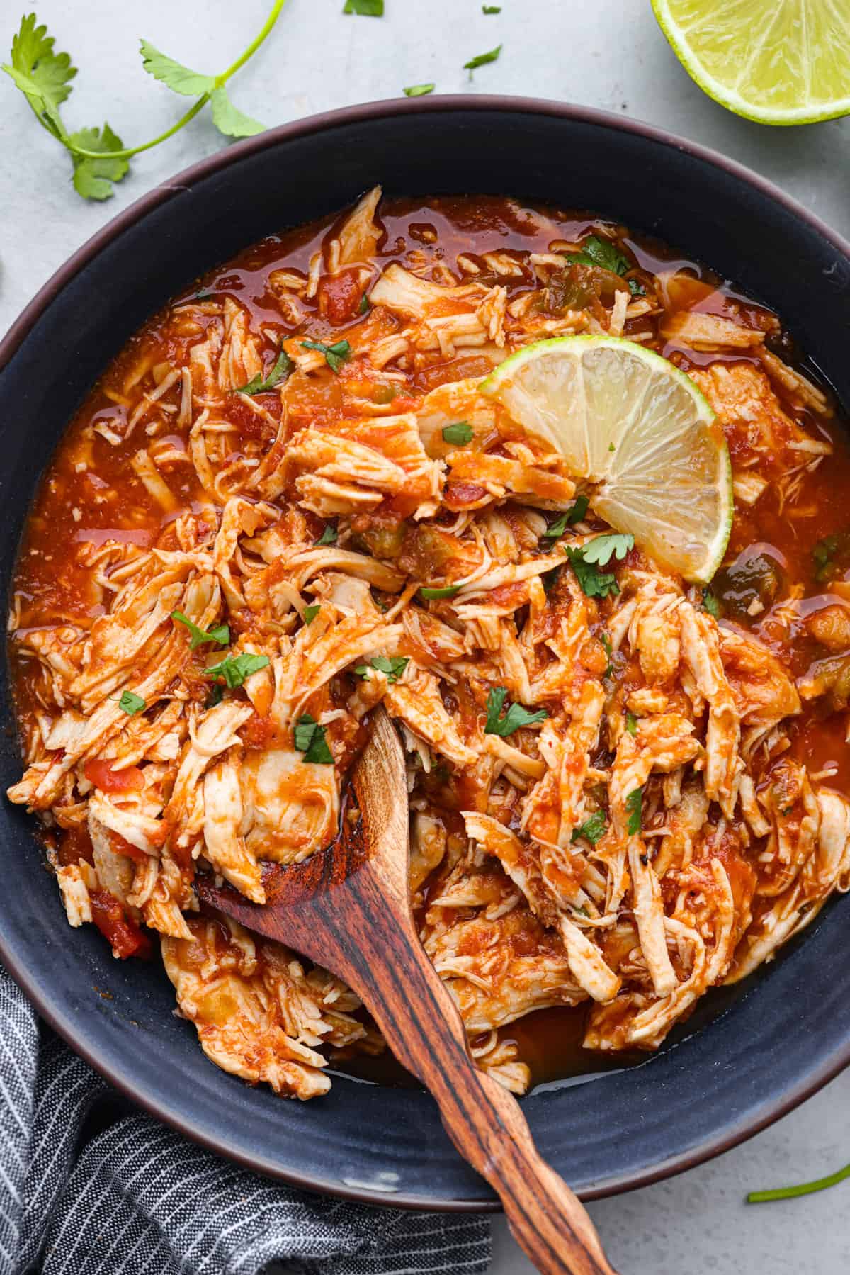 Weeknight dinner made easy with this crockpot salsa chicken! Tender flavorful chicken that only takes 5 ingredients to make. It's a versatile recipe the whole family will love! Chicken in a black bowl with a wood serving spoon and garnished with limes.