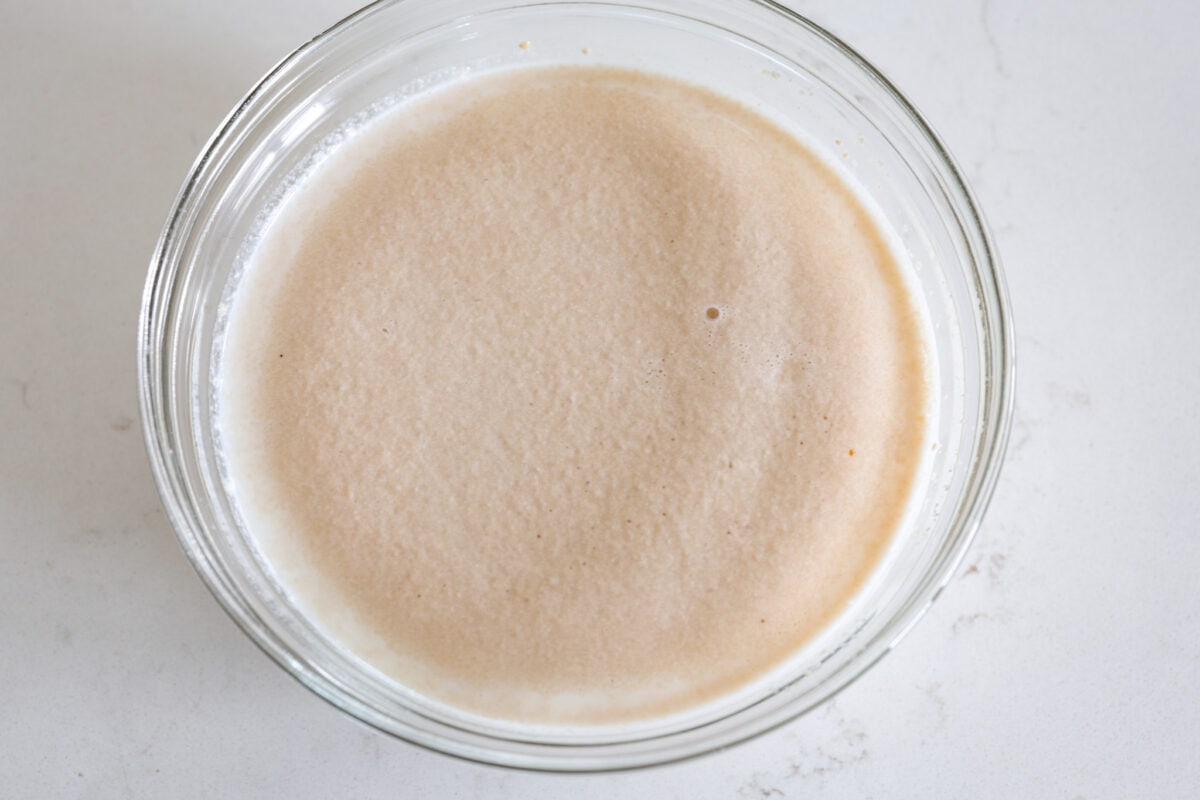 First process photo of milk, sugar, and yeast proofing in a bowl. 