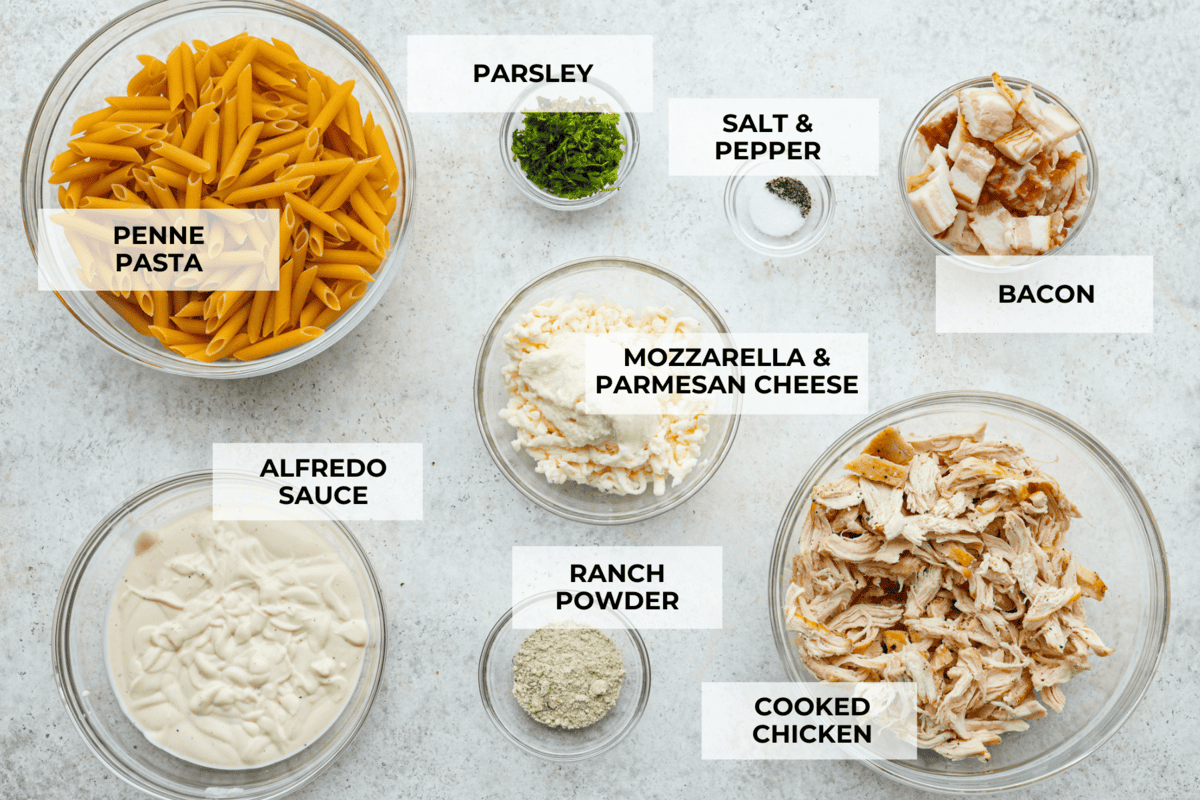 Chicken Bacon Ranch Casserole is a meal the whole family will gobble up in no time! It's super easy to make with a mix of pasta, bacon, shredded chicken, creamy ranch sauce and plenty of cheese. An irresistible dinner that's simple enough for busy weeknights! The top view of each ingredient in a glass bowl and labeled.