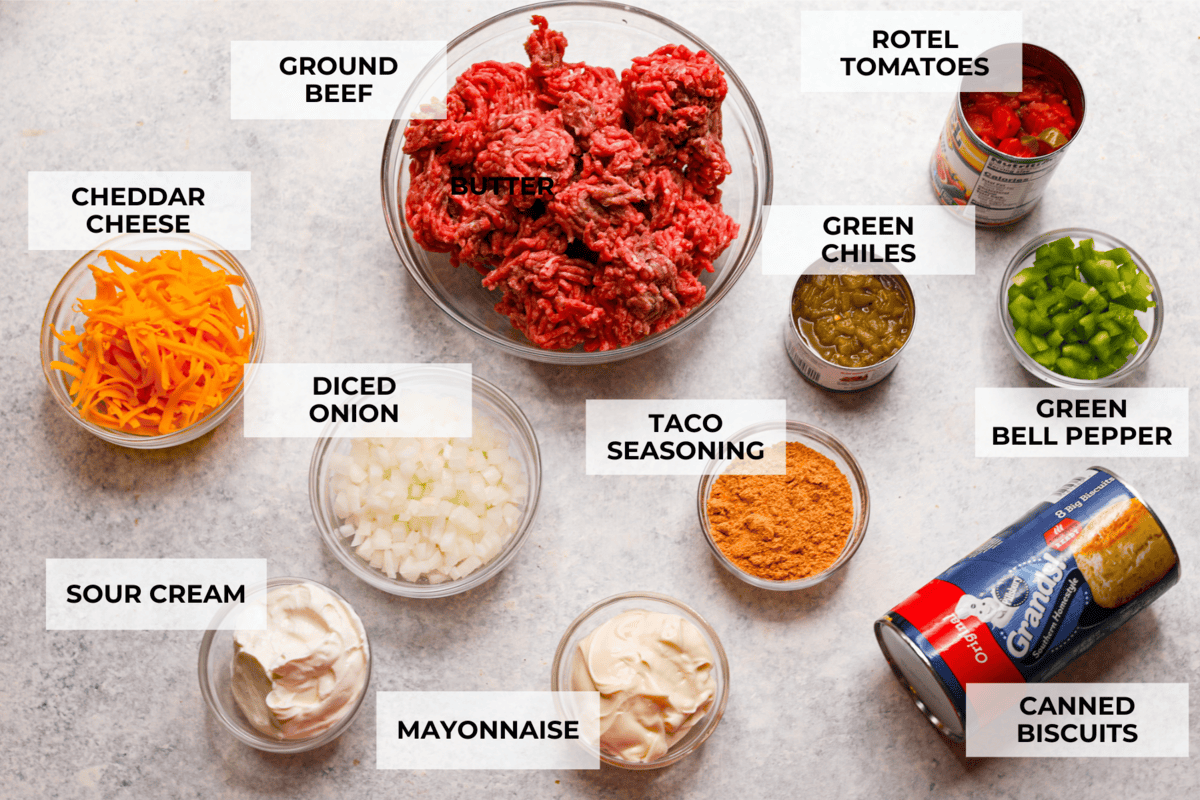 This delicious John Wayne Casserole is Mexican comfort food at its finest! Layers of seasoned ground beef, creamy cheddar cheese mixture, and more shredded cheese are baked on top of a biscuit crust for a crowd-pleasing family dinner! A top view of the ingredients laid out in individual glass bowls and each labeled.