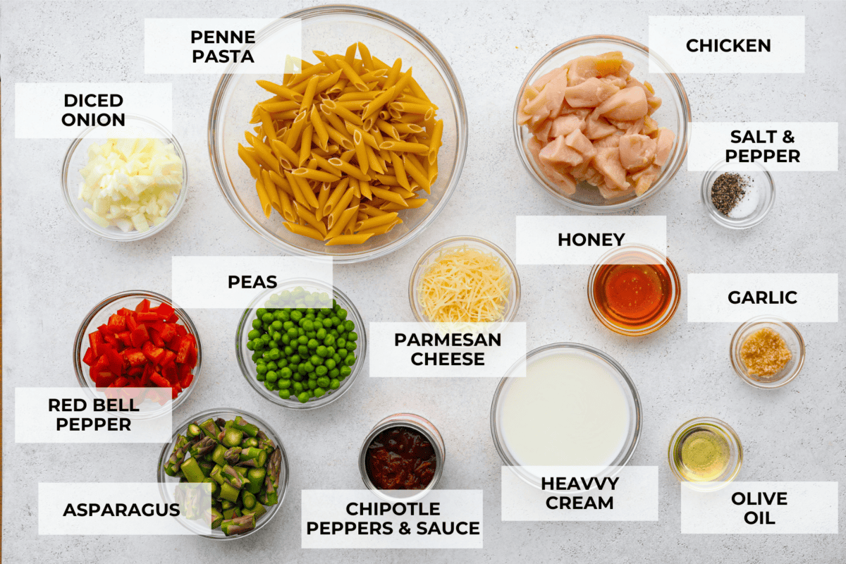 All of the ingredients for the chipotle pasta separated into glass bowls. Listed are: diced onion, penne pasta, chicken, salt and pepper, red bell pepper, peas, parmesan cheese, honey, garlic, asparagus, chipotle peppers, heavy cream, and olive oil.
