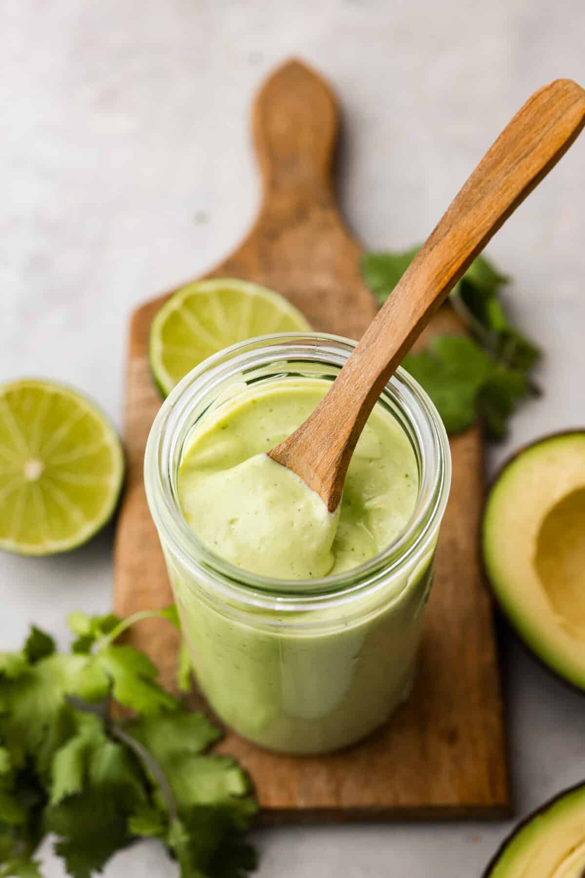 Overhead view of avocado dressing in glass jar with wood spoon sticking out. 