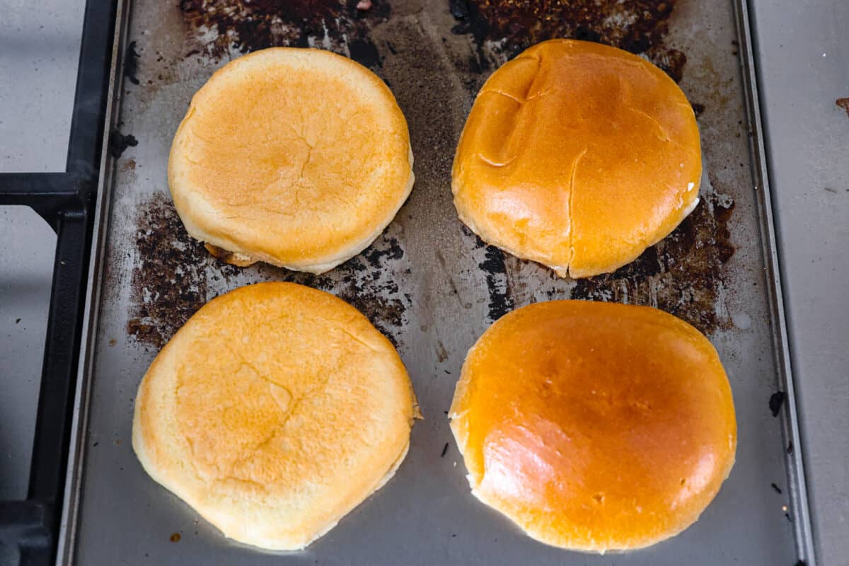 Overhead view of hamburger buns on a griddle being toasted. 