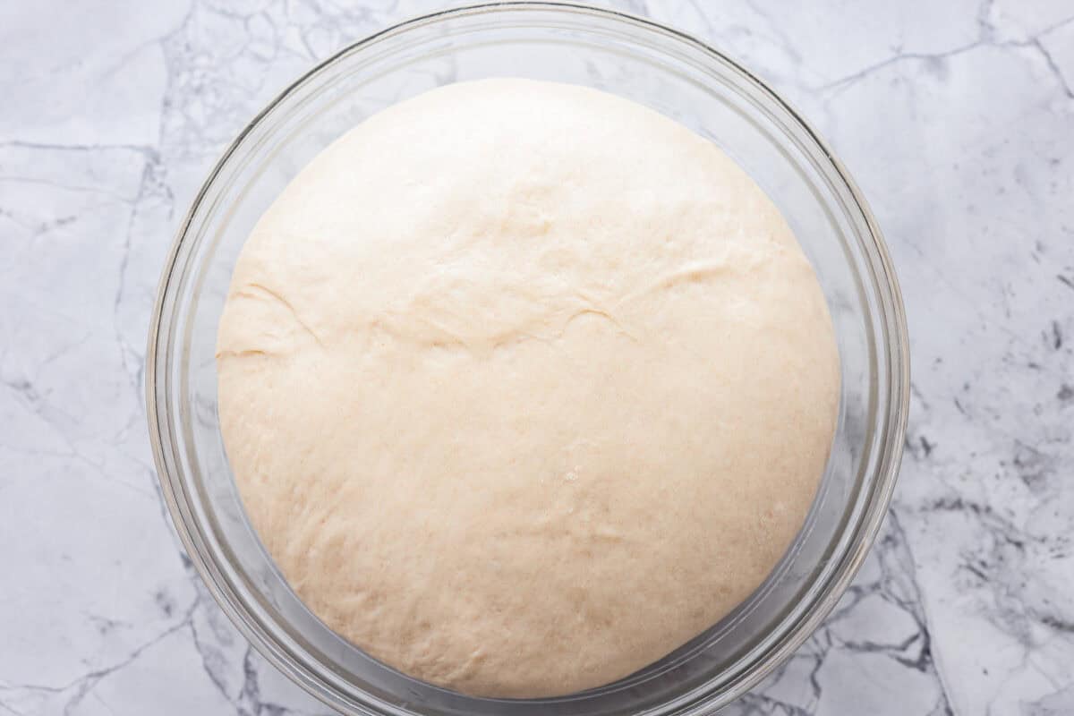 A picture of properly proofed dough in a clear glass bowl showing how to bake with yeast. 