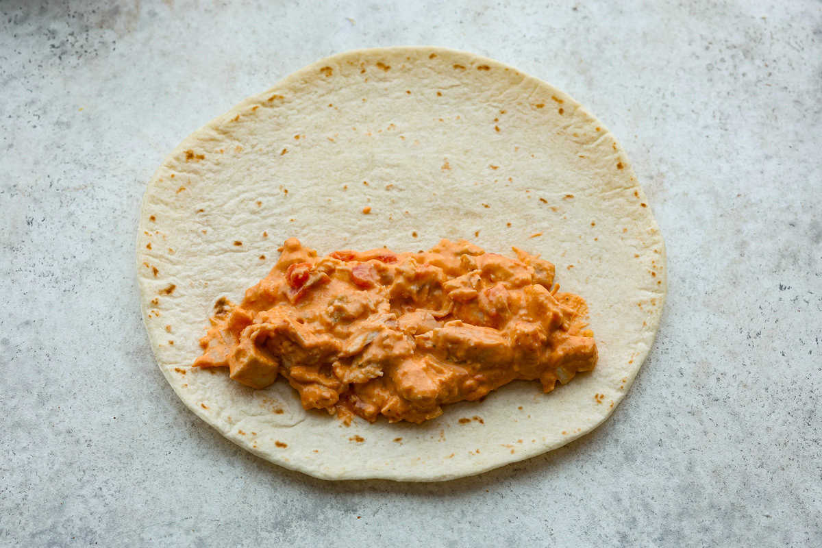 A new enchilada is in town! Get ready for the bold flavors in these buffalo chicken enchiladas! Chicken enchiladas loaded with cheese and smothered in a creamy buffalo enchilada sauce. Fifth photo of the chicken added to the tortillas.