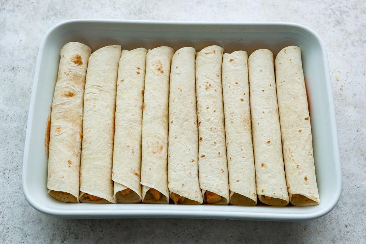 A new enchilada is in town! Get ready for the bold flavors in these buffalo chicken enchiladas! Chicken enchiladas loaded with cheese and smothered in a creamy buffalo enchilada sauce. Sixth photo of the enchiladas layered in the baking dish.