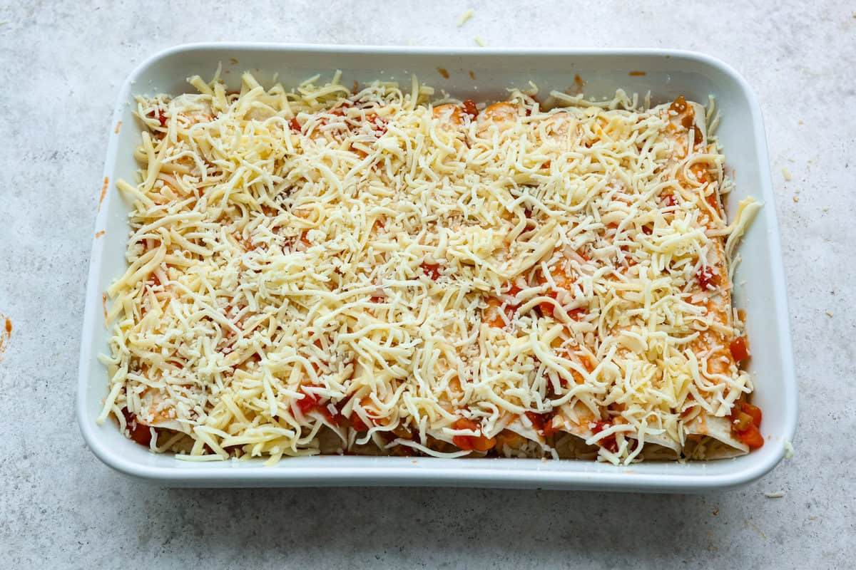 A new enchilada is in town! Get ready for the bold flavors in these buffalo chicken enchiladas! Chicken enchiladas loaded with cheese and smothered in a creamy buffalo enchilada sauce. Eighth photo of the cheese sprinkled on top of the buffalo chicken enchiladas before baking.