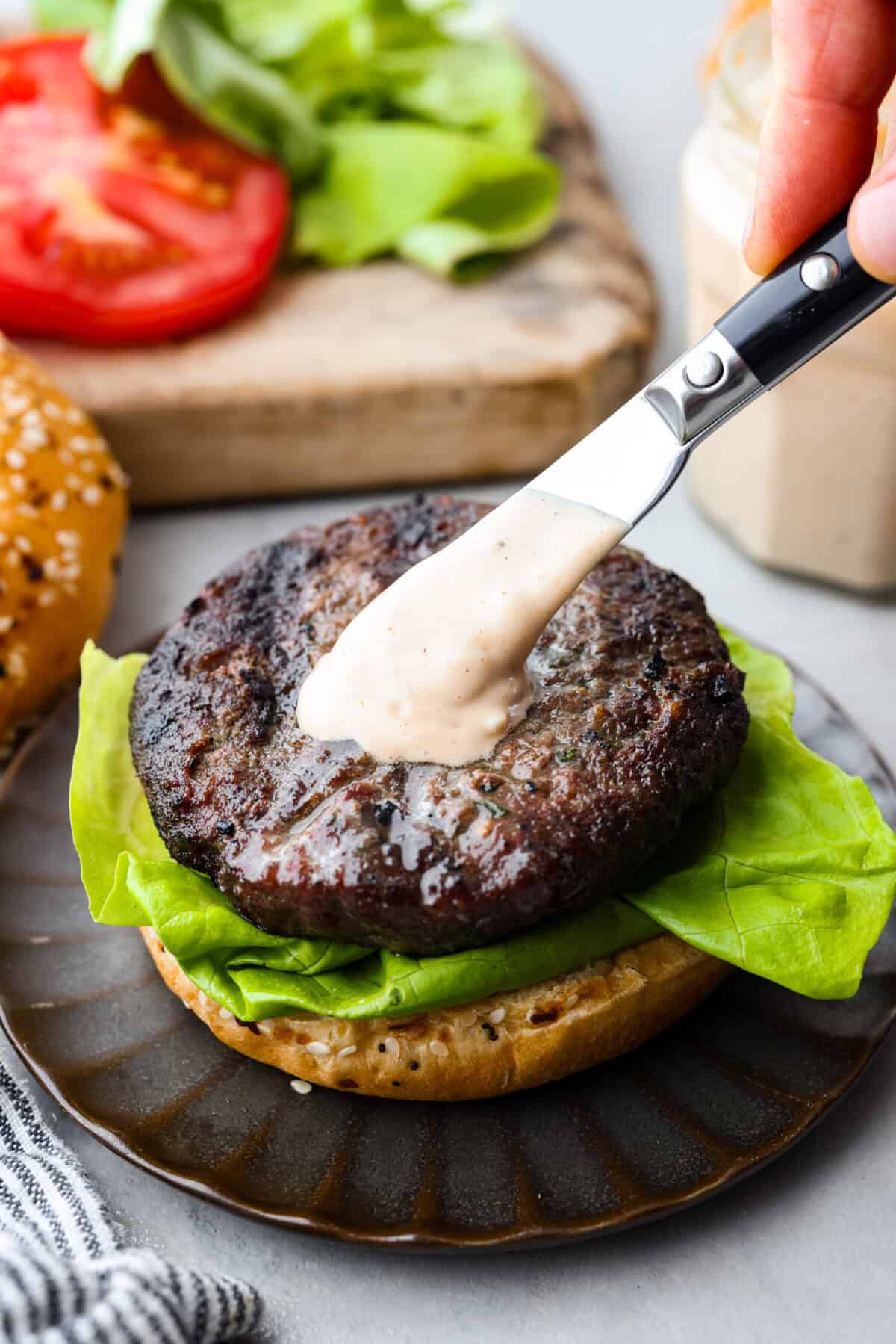 Burger sauce being spread onto a patty that is on a bun with lettuce. 