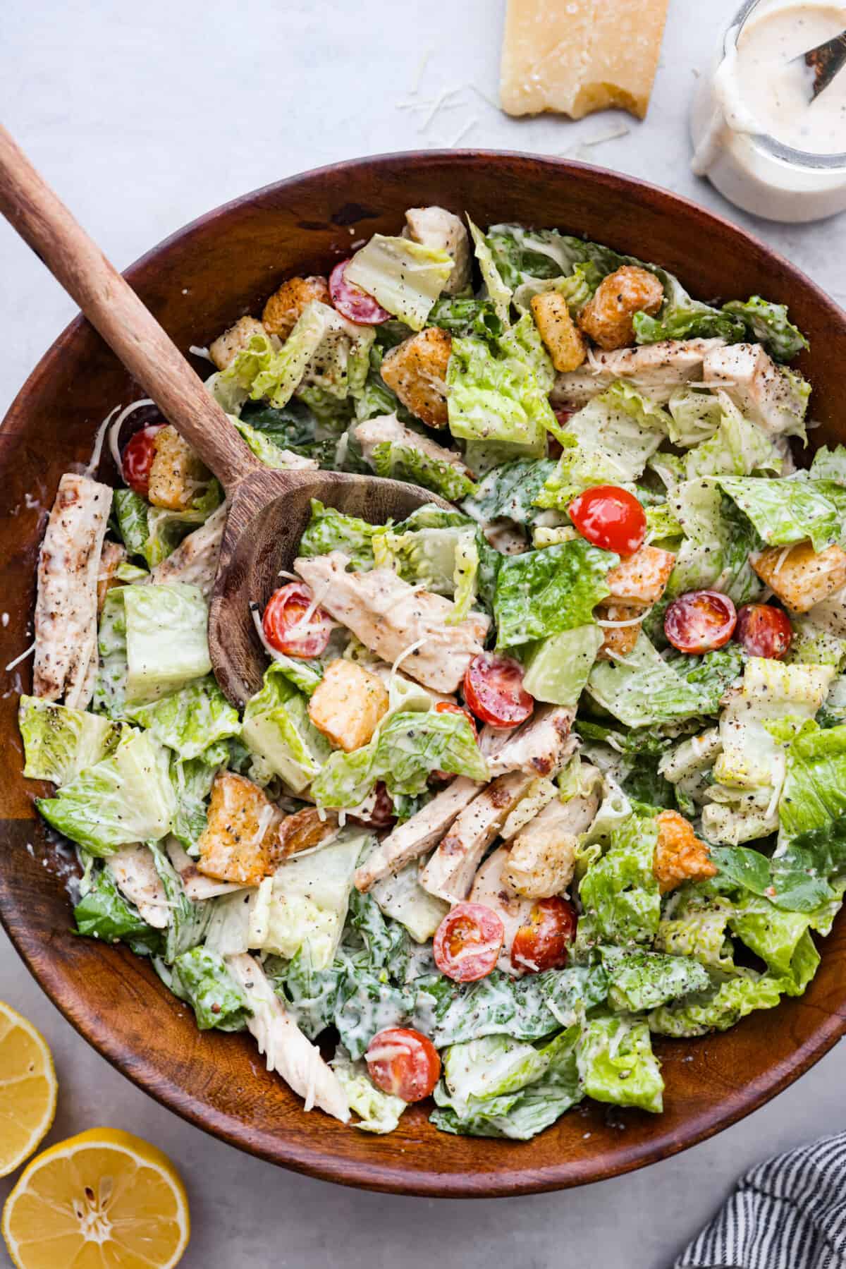 Top view of a chicken caesar salad in a wooden bowl with a wooden spoon in it. 