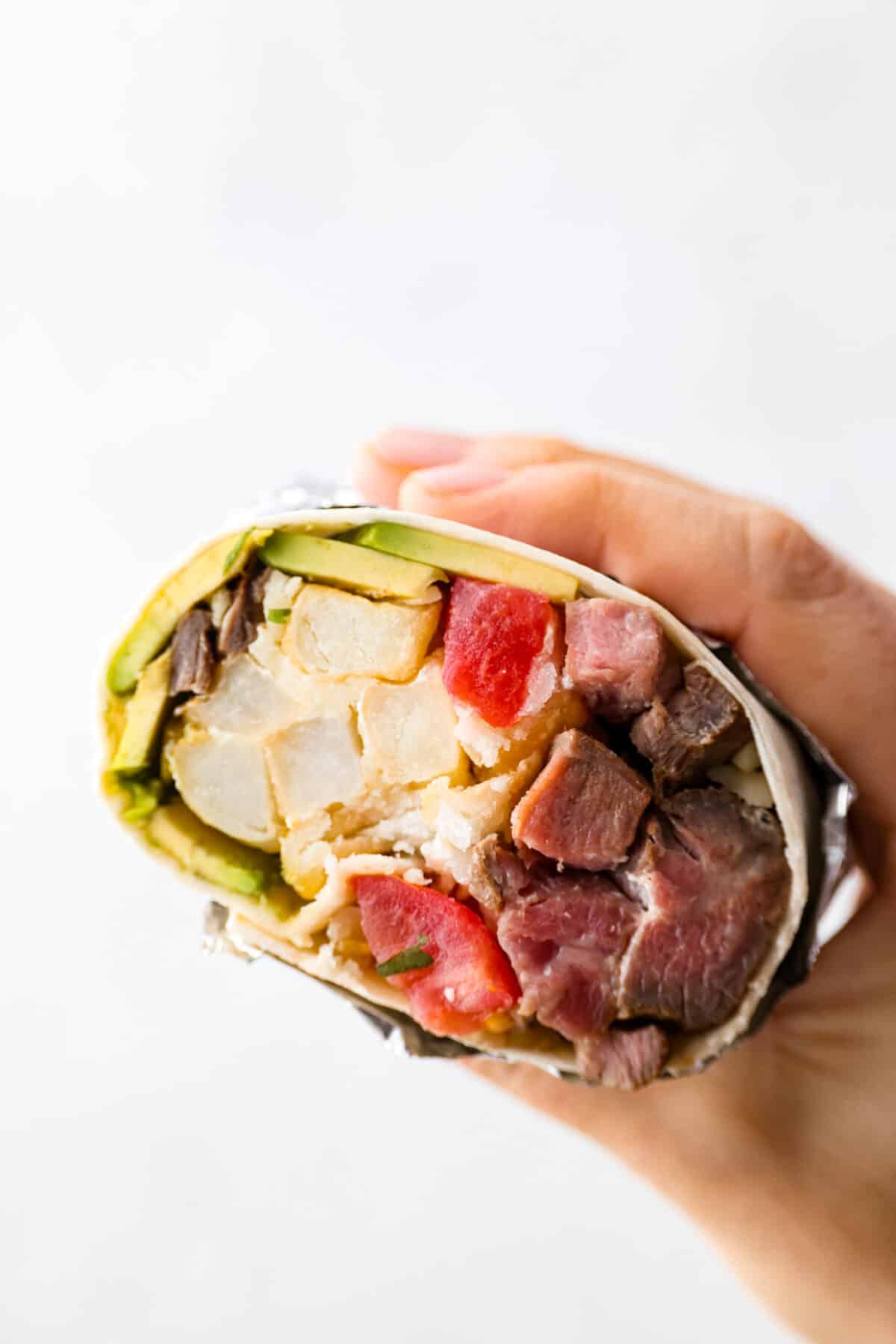 A half holding a California burrito that is sliced open so that you can see the inside. 