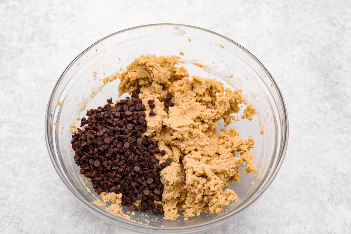 I am so excited about this recipe, it combines two of my all-time favorite desserts, cookie dough and cheesecake! With the rich Oreo crust, creamy cheesecake filling, and edible cookie dough bites, this no-bake cookie dough cheesecake will have your taste buds begging for more! Overhead shot of a bowl with mixed ingredients and mini chocolate chips.