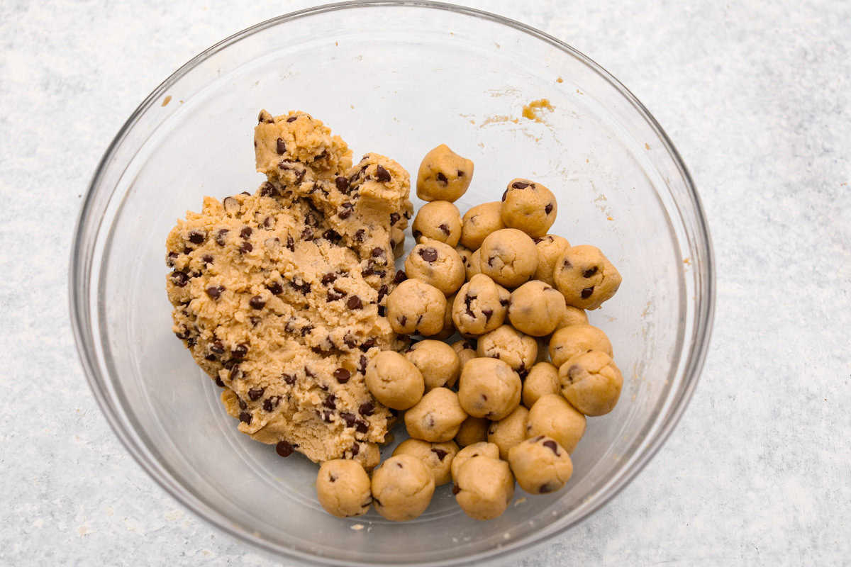 I am so excited about this recipe, it combines two of my all-time favorite desserts, cookie dough and cheesecake! With the rich Oreo crust, creamy cheesecake filling, and edible cookie dough bites, this no-bake cookie dough cheesecake will have your taste buds begging for more! Overhead shot of a bowl with cookie dough, and balls of cookie dough.